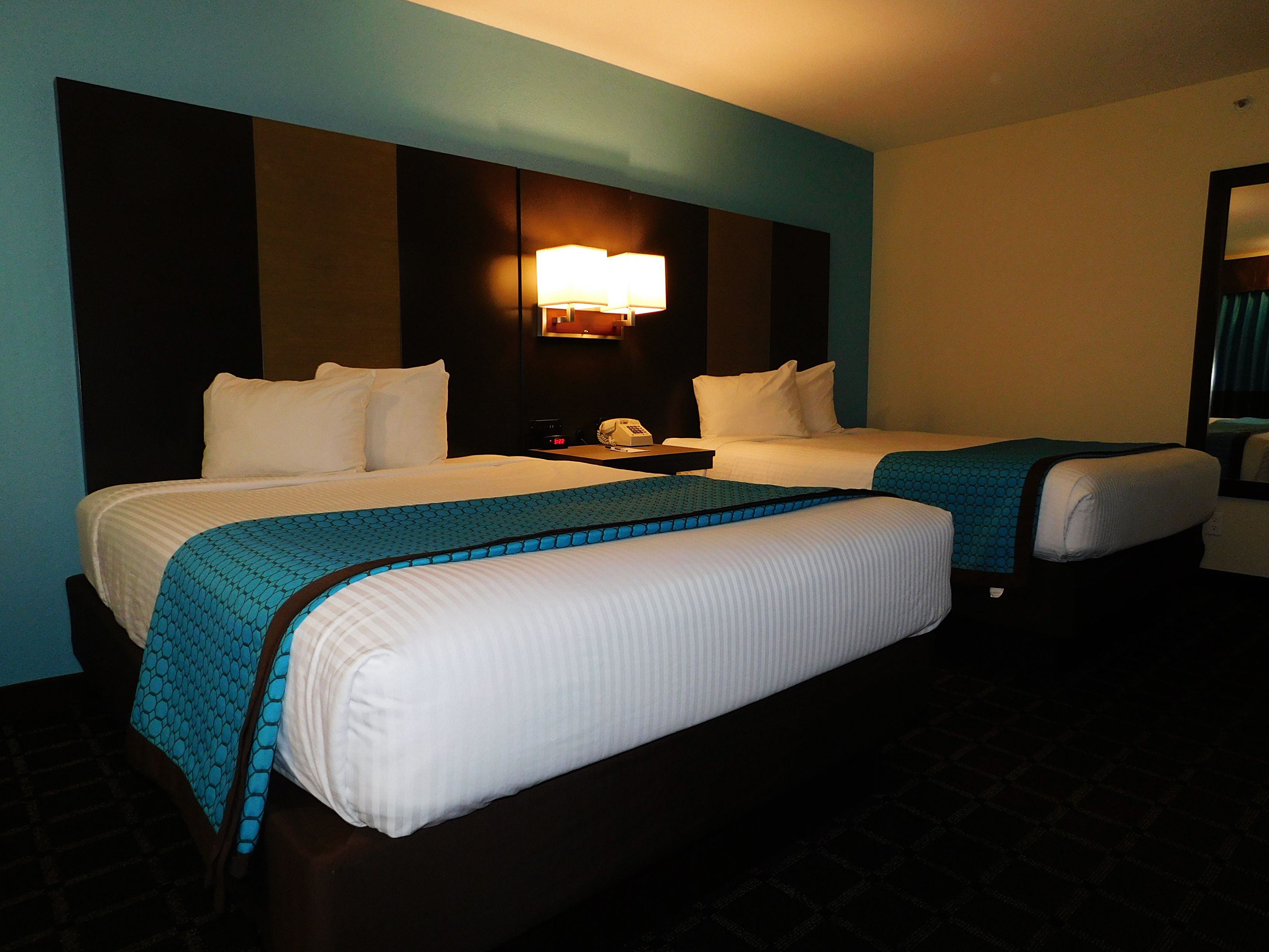 A hotel room with two beds, a nightstand, a lamp, and a window with curtains.