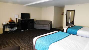 A hotel room with two beds, a desk with a computer, a television, and a sofa.
