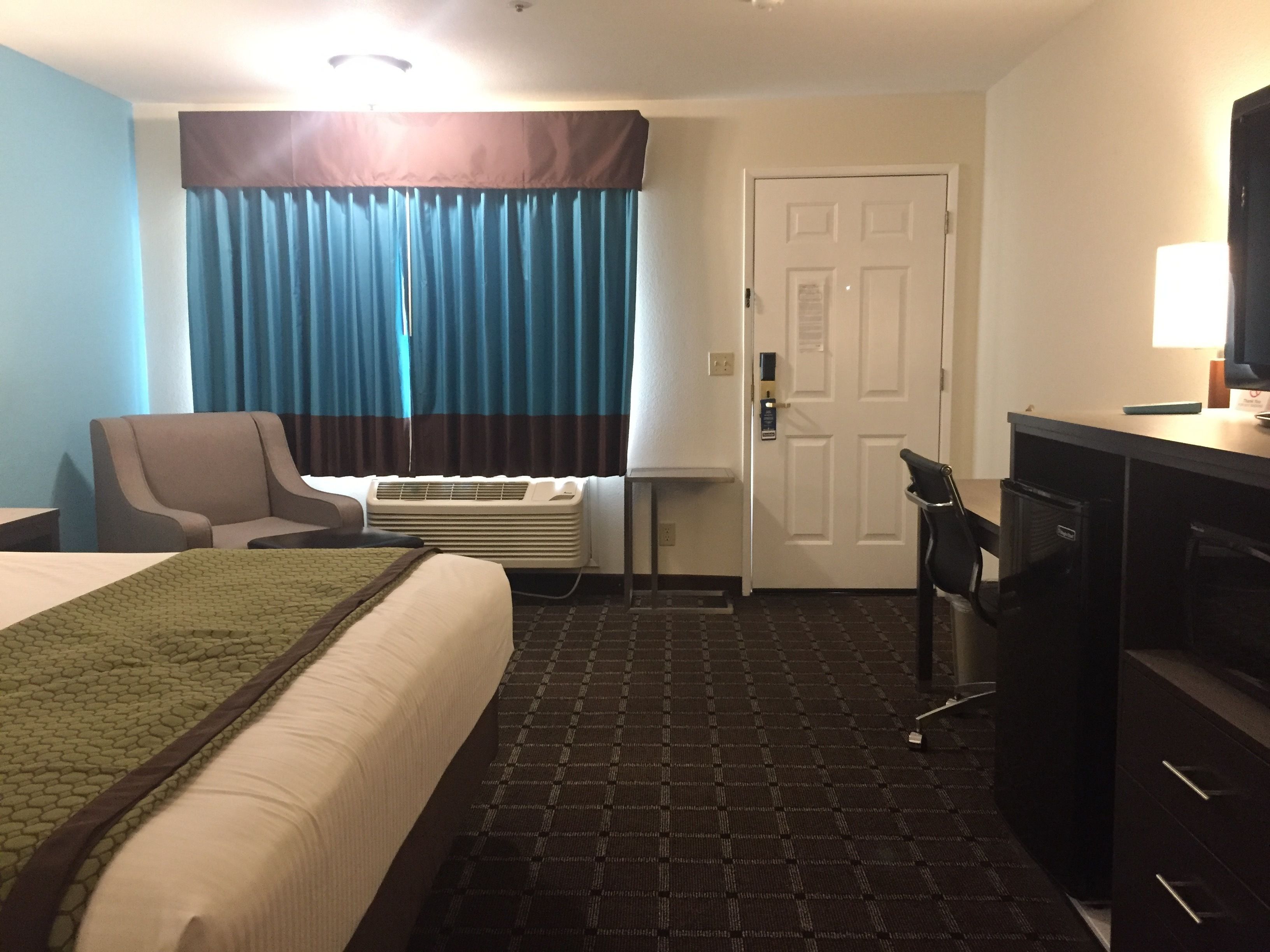 A hotel room with a bed, a chair, a desk, a television, and a door.