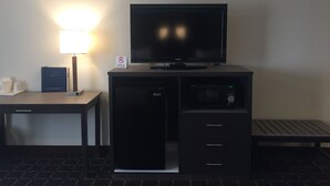 Hotelkamer met een flatscreen televisie op een zwarte entertainmentkast, een bureau met een lamp, een kleine koelkast en een magnetron.