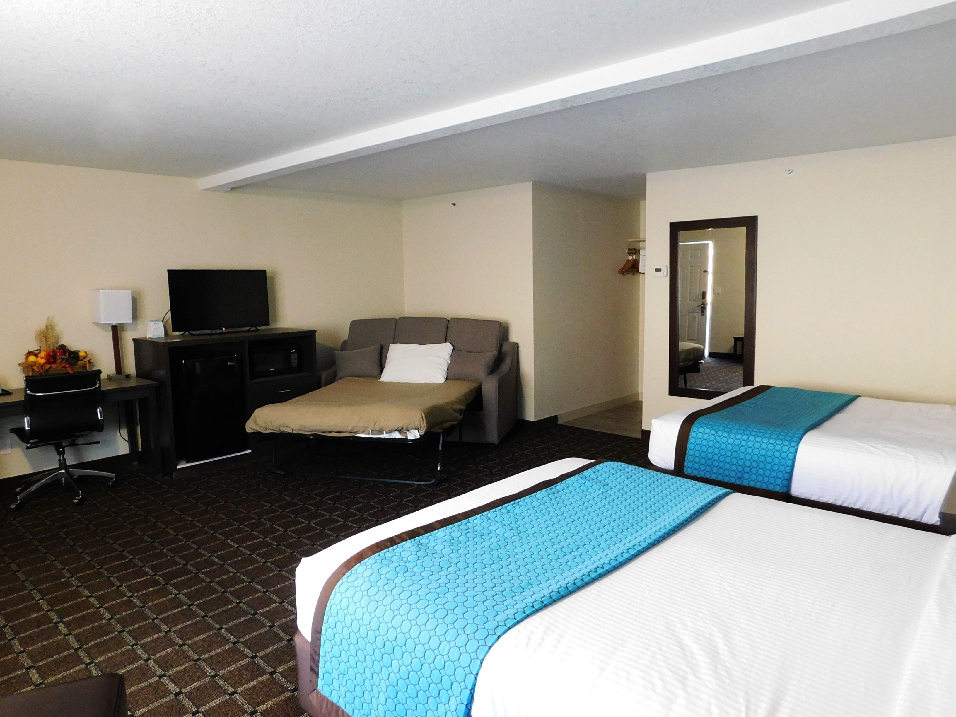 A hotel room with a bed, a desk with a television, and a mirror.