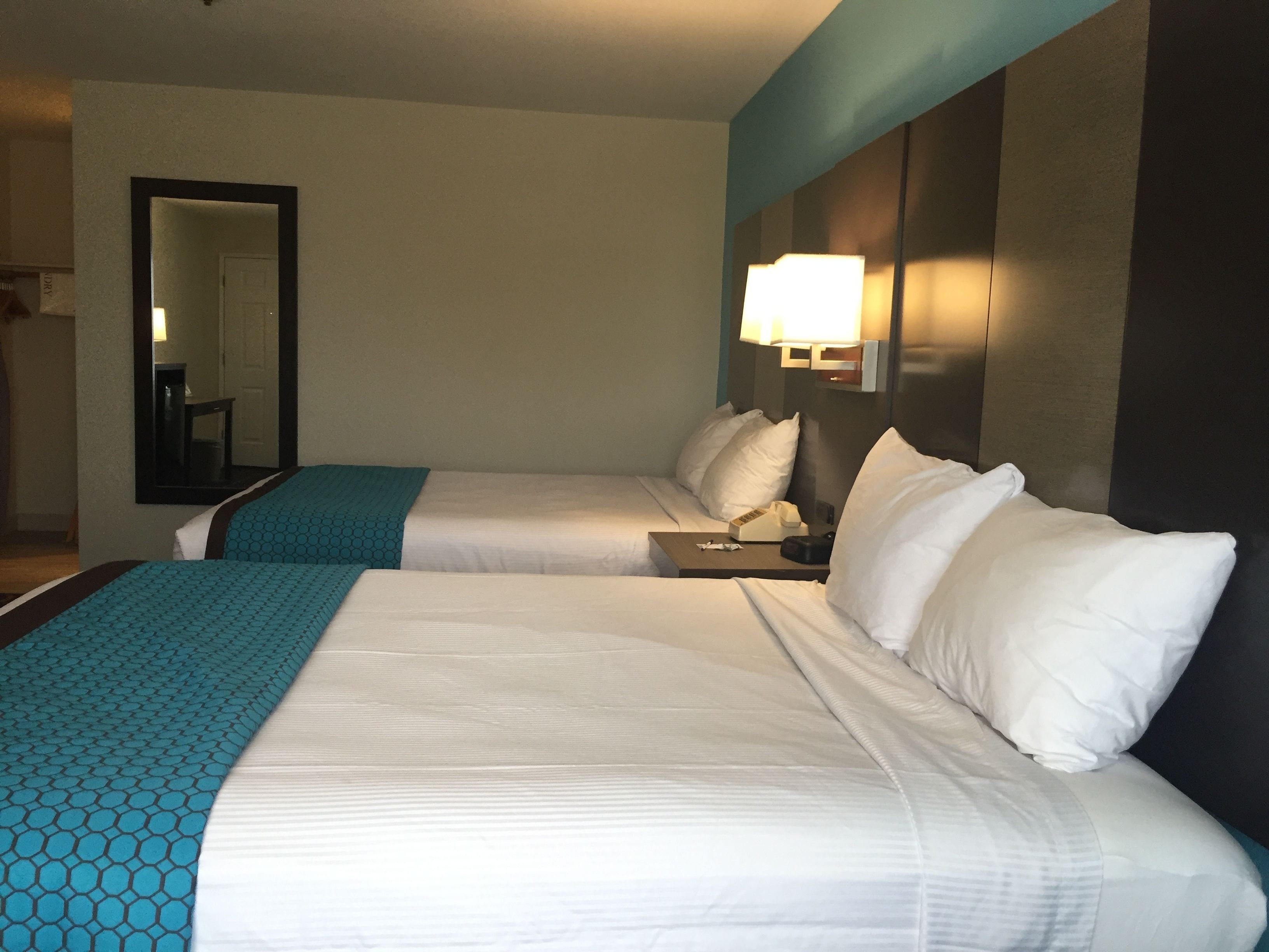 A hotel room with two beds, a nightstand, a lamp, and a mirror.