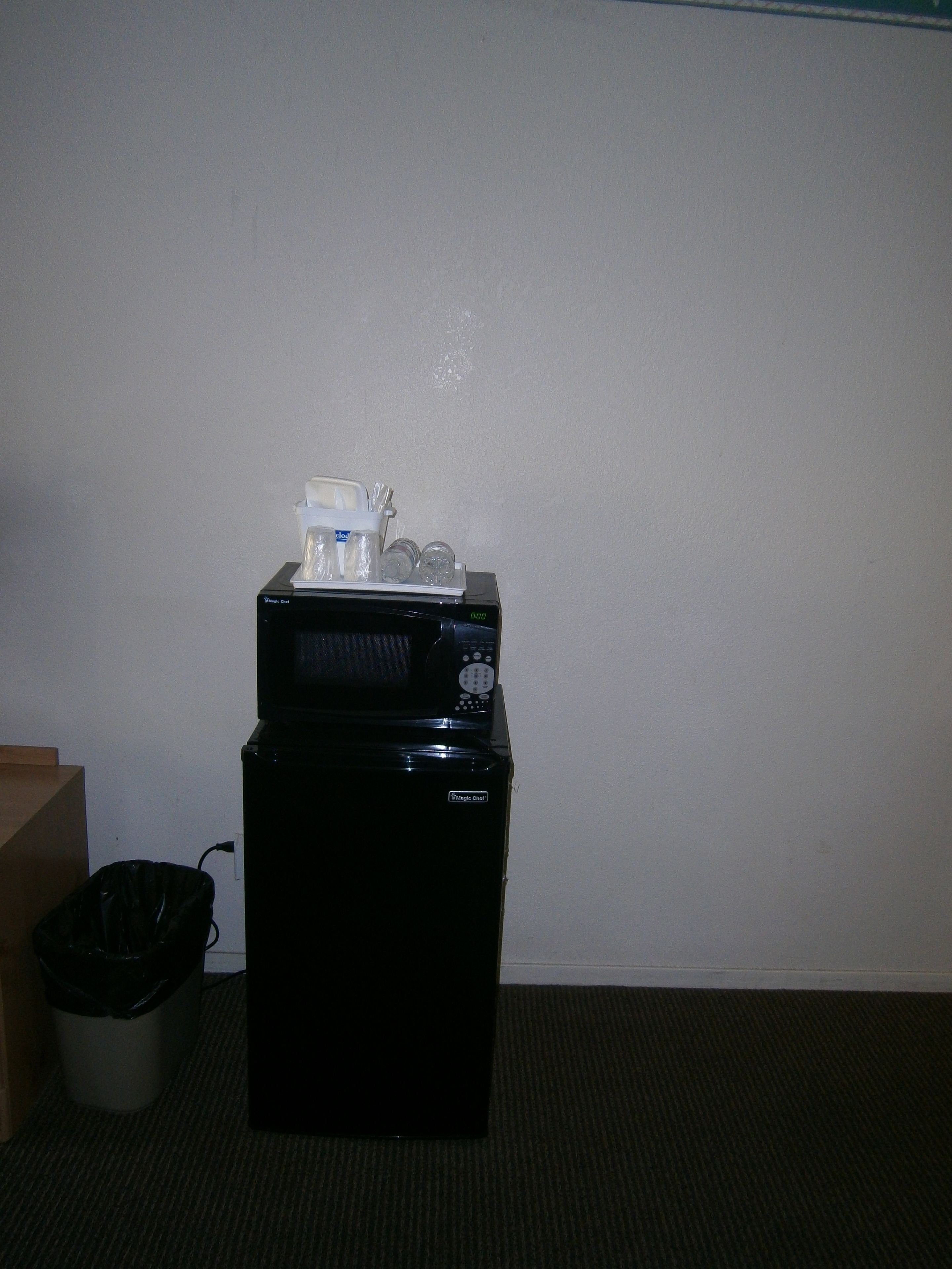 A microwave with a digital display and a control panel, placed on a black surface against a plain wall.