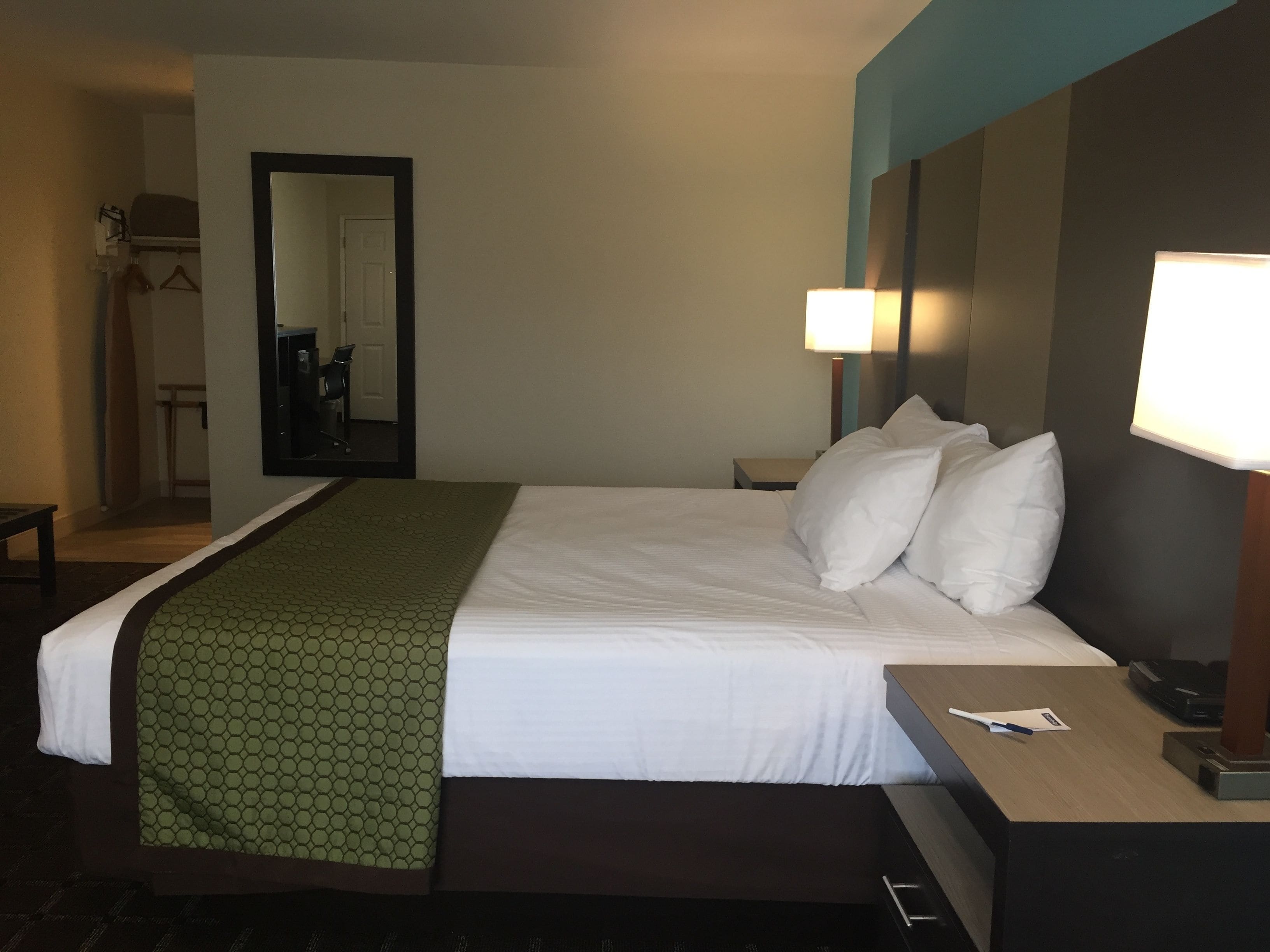 A hotel room with a large bed, a bedside table, a nightstand, a lamp, and a mirror.
