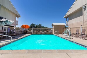 Ein Swimmingpool mit Liegestühlen und Sonnenschirmen, umgeben von Gebäuden.