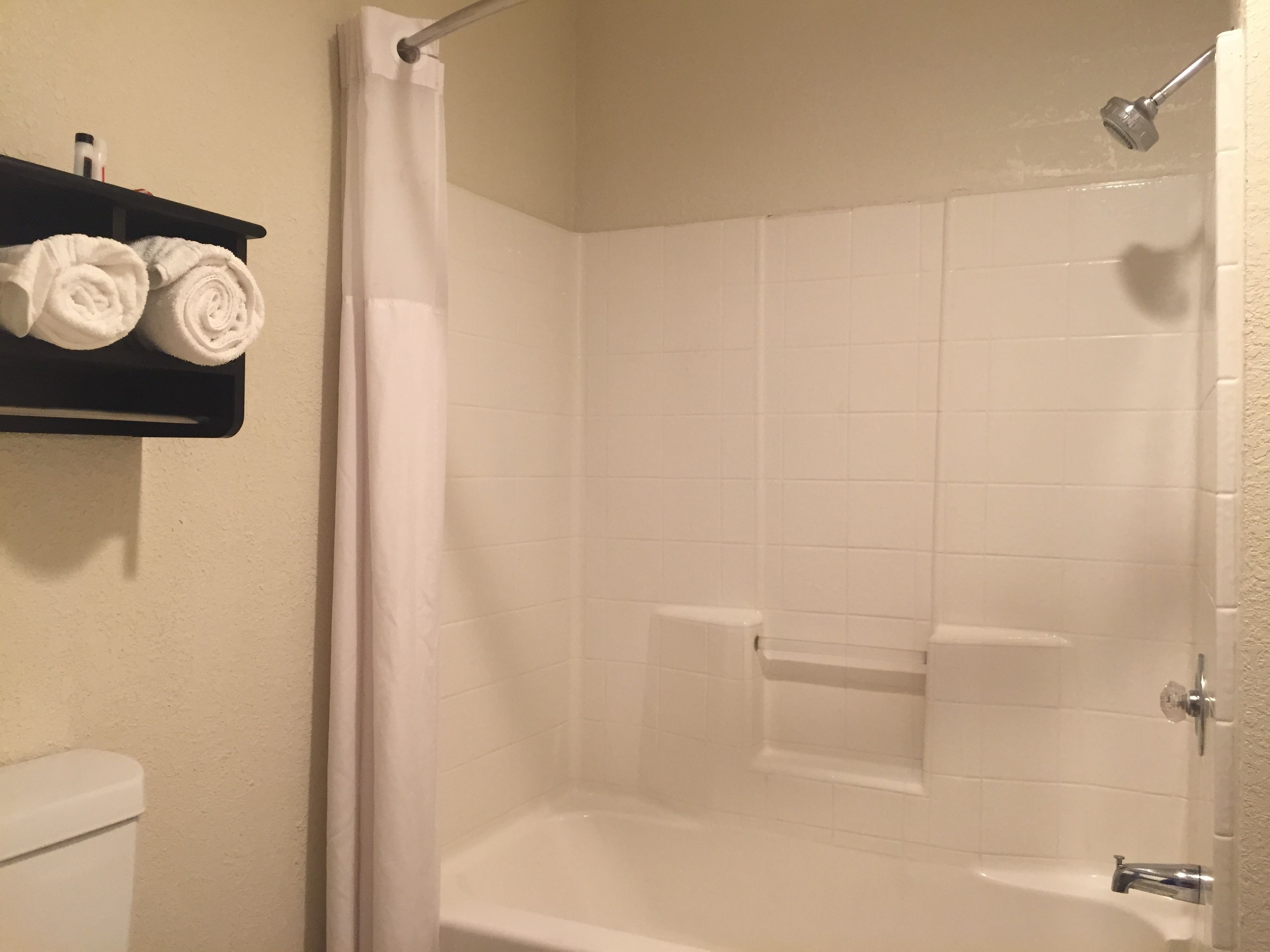 A bathroom with a white bathtub, a shower curtain, and a shelf with two rolled towels.