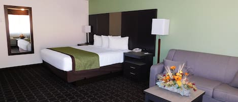 A hotel room with a bed, a nightstand, a lamp, a sofa, and a table with flowers.