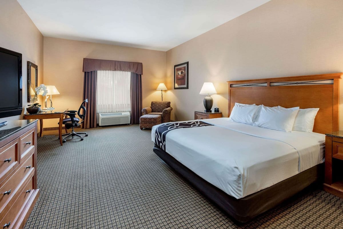 Een hotelkamer met een groot bed, een bureau met stoel, een televisie, een lamp en een raam met gordijnen.