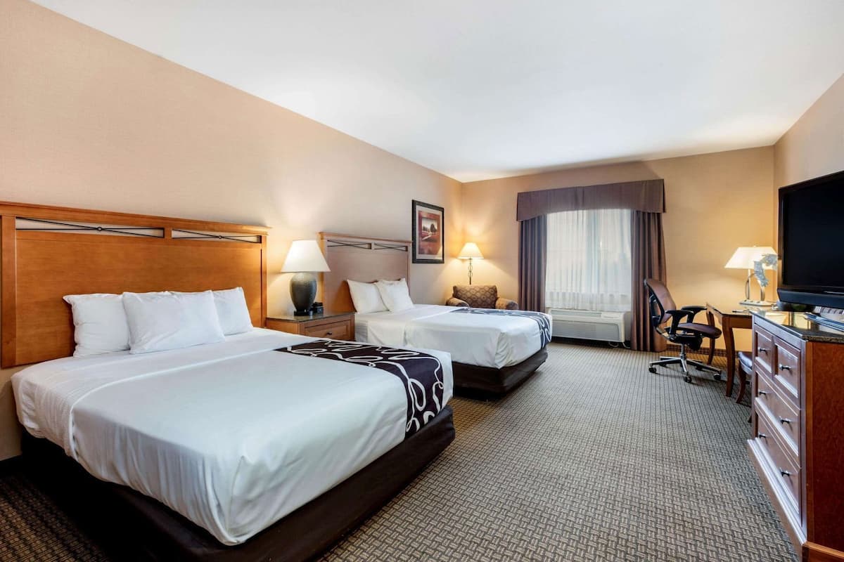 Een hotelkamer met twee bedden, een bureau, een stoel, een televisie en een raam met gordijnen.