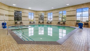 A large indoor swimming pool with multiple lanes, surrounded by chairs and benches, and large windows offering views of the outside.
