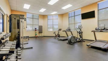 Una palestra con diverse attrezzature per esercizi, ampie finestre e una lavagna a parete.
