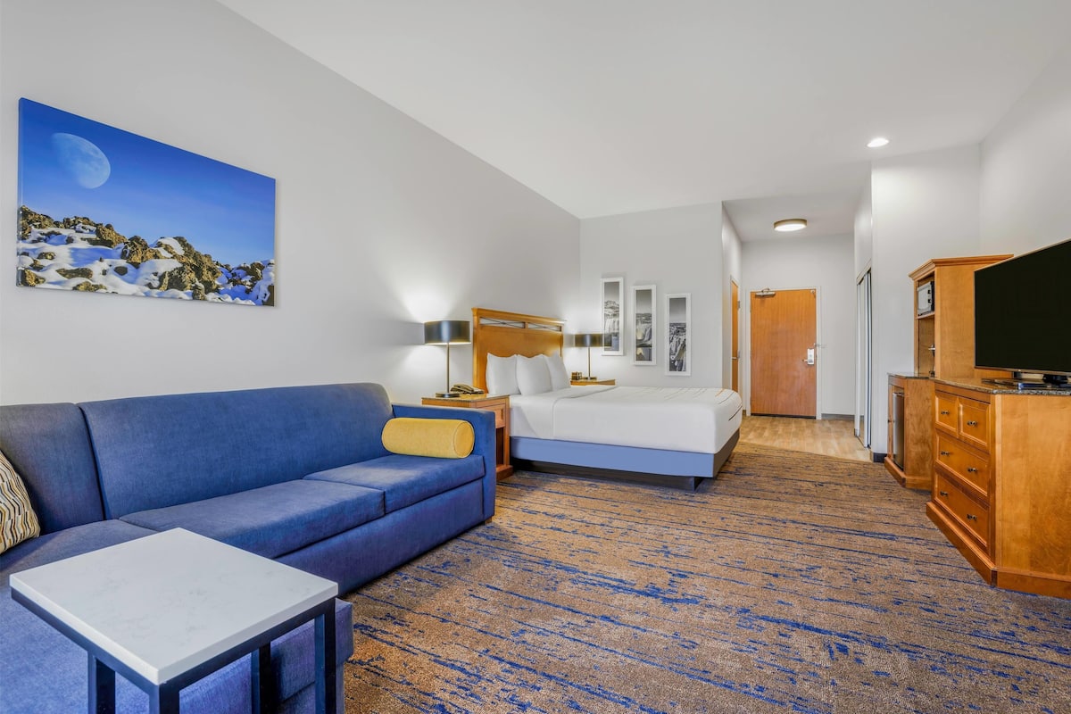 Een hotelkamer met een blauwe bank, een bed, een televisie en een schilderij van een maanverlicht landschap.