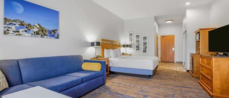 Une chambre d’hôtel avec un canapé bleu, un lit, une télévision et un tableau représentant un paysage éclairé par la lune.