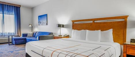 A hotel room with a large bed, a sofa, a desk, and a lamp.