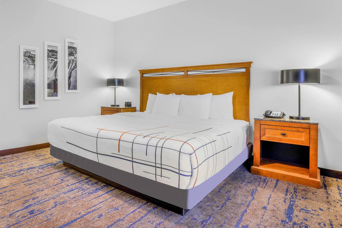 Een hotelkamer met een groot bed, twee nachtkastjes met lampen, een houten hoofdbord en een kamerbreed tapijt met dessin.