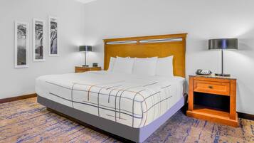Une chambre d’hôtel avec un grand lit, deux tables de chevet avec des lampes, une tête de lit en bois et une moquette à motifs.