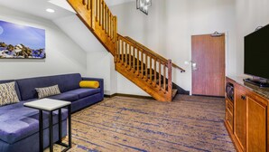 A living room with a blue sofa, a small table, a wooden staircase, a television, and a door.