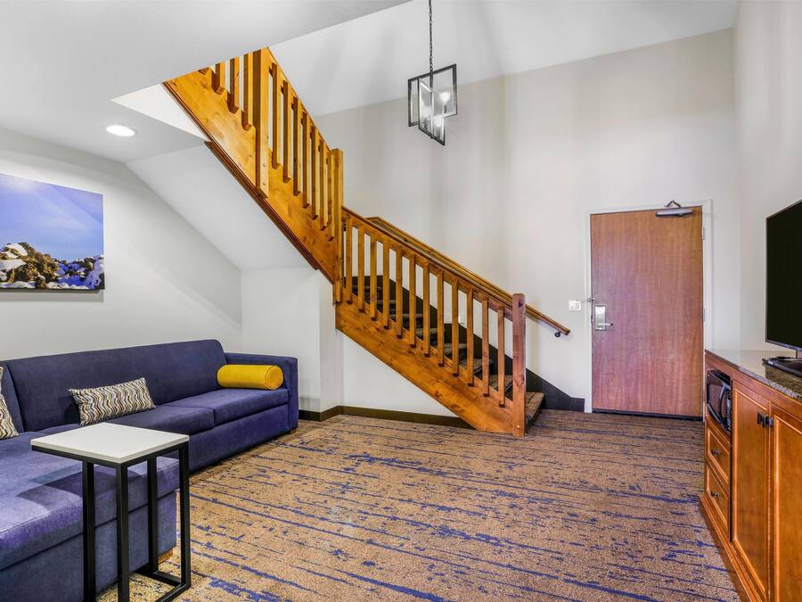 A living room with a blue sofa, a small table, a wooden staircase, a television, and a door.