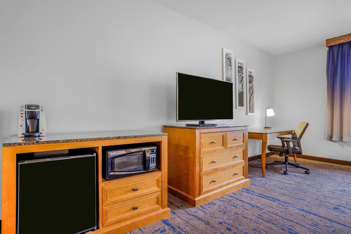 Een hotelkamer met een houten bureau, een televisie, een magnetron, een koffiezetapparaat en een stoel.