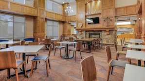 A spacious dining area with high wooden walls, multiple tables and chairs, a stone fireplace, and hanging pendant lights.