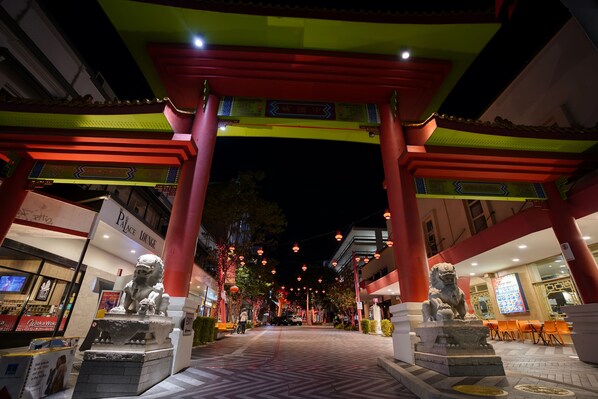Una puerta tradicional china con estatuas de leones, un letrero de neón y un edificio moderno al fondo.