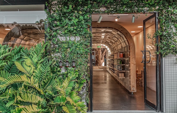 A store entrance with a green leafy archway, a wooden interior, and a visible exit sign.