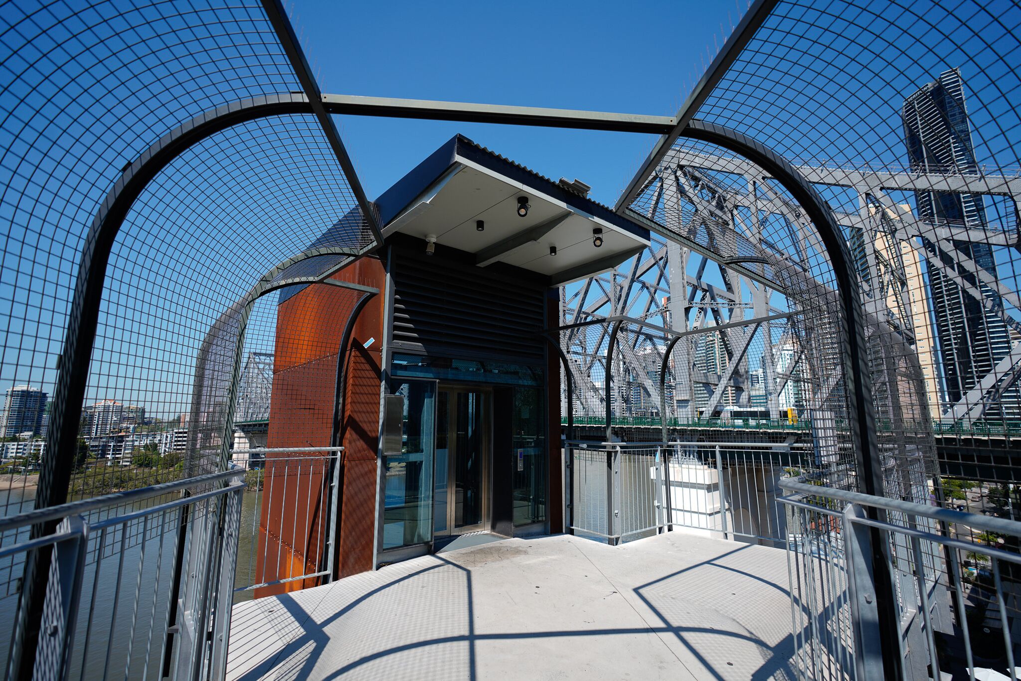 A modern building with a glass entrance, metal framework, and a view of a bridge and cityscape.