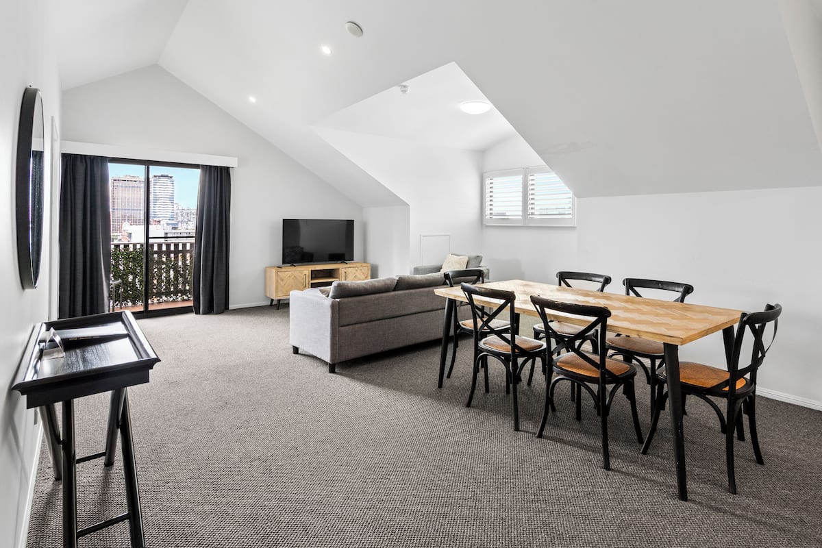 A modern loft apartment with a dining area, sofa, TV, and city views.