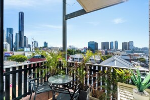A balcony with a table and chairs, overlooking a cityscape with various buildings.