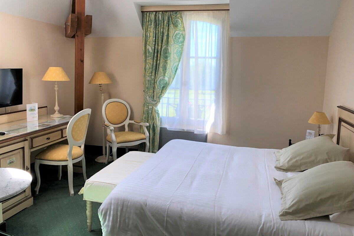 A hotel room with a bed, two chairs, a desk, a television, and two lamps.
