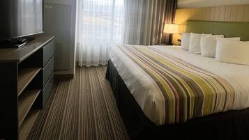Quarto de hotel com uma cama grande, televisão em móvel, escrivaninha e janela com cortinas.