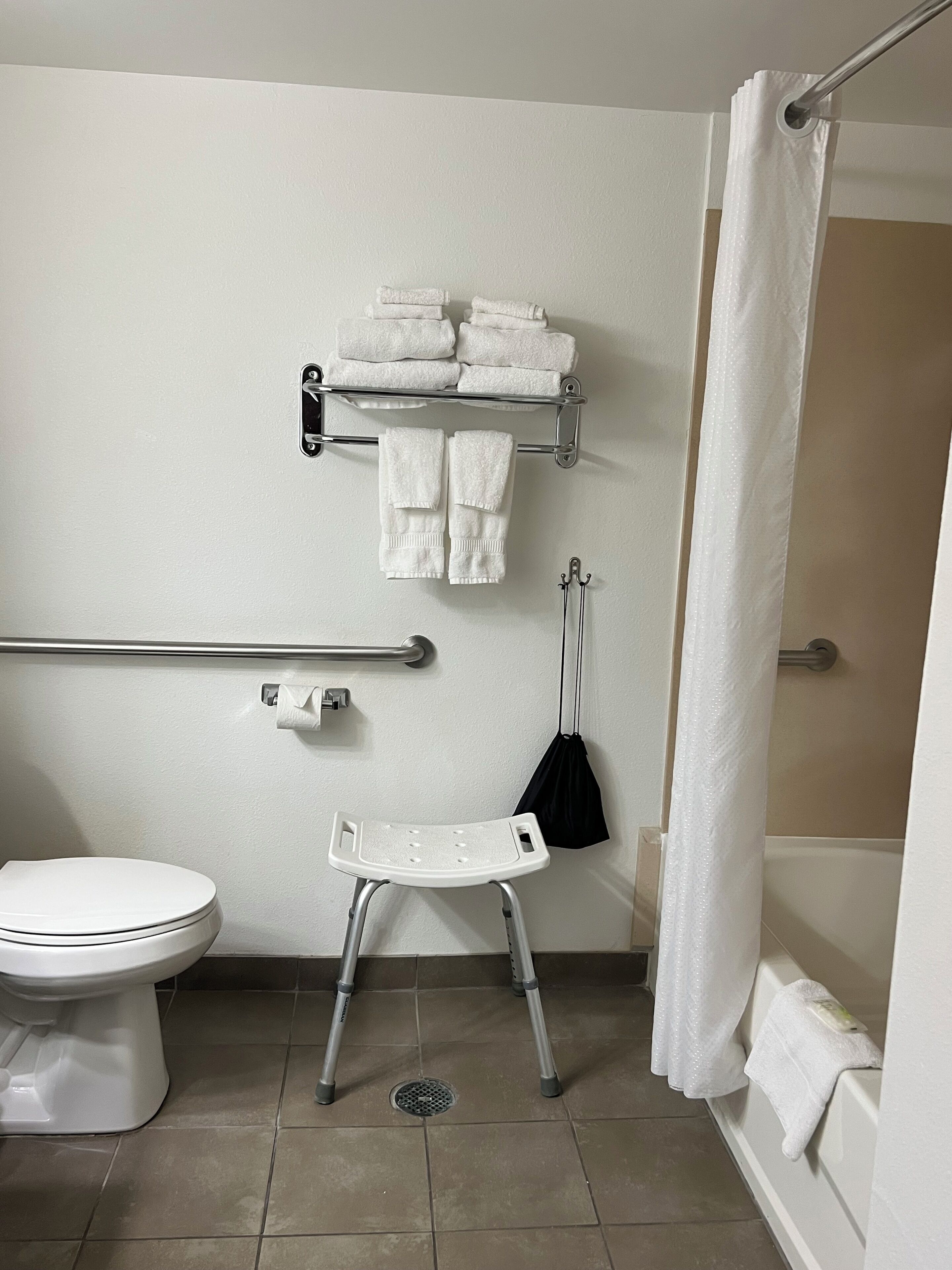 A bathroom with a white toilet, a white sink, a grab bar, a white shower curtain, and a white towel rack.