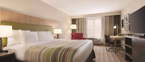 A hotel room with a bed, a desk, a chair, a TV, and a window with curtains.