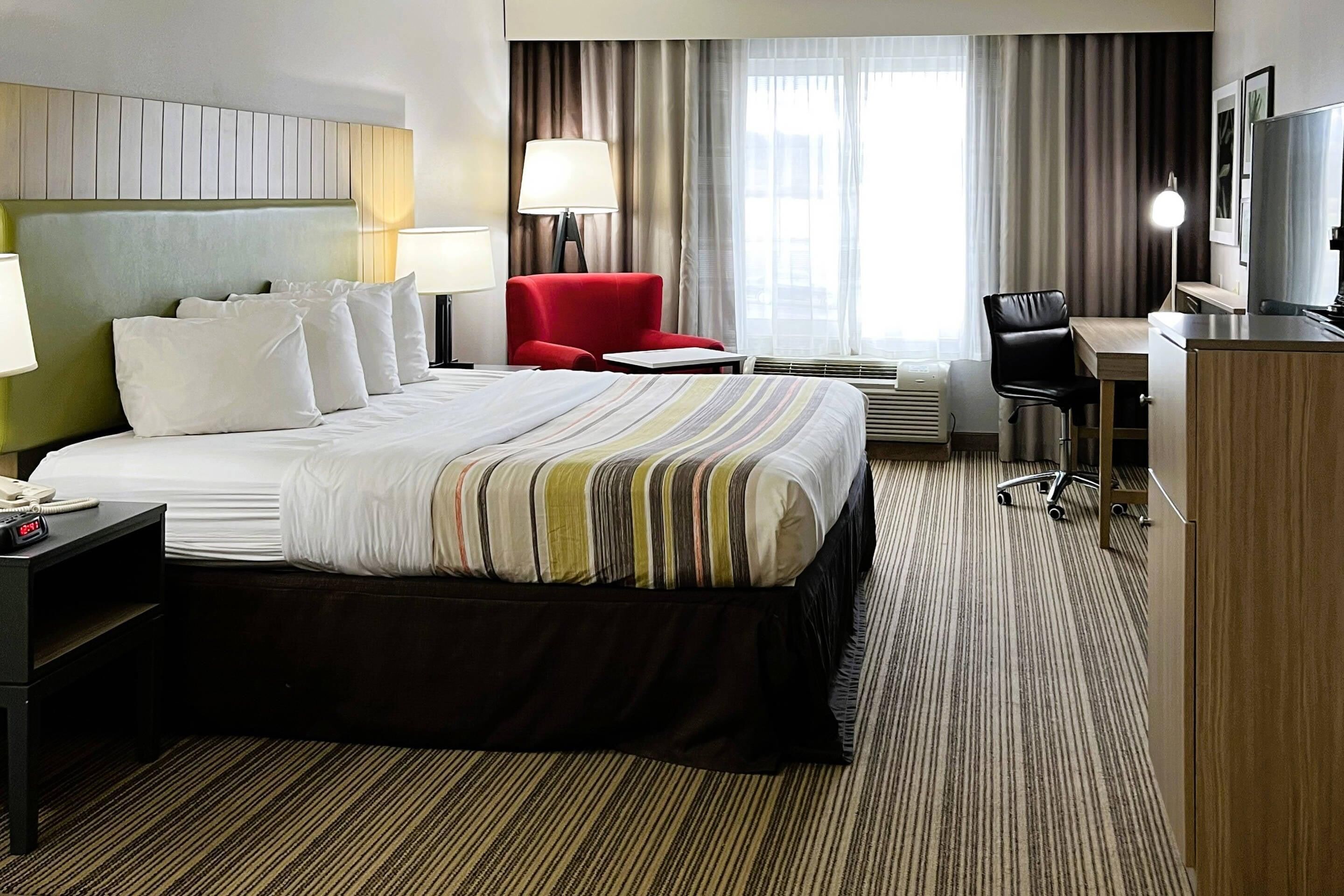 A hotel room with a bed, a desk, a chair, a TV, and a lamp.
