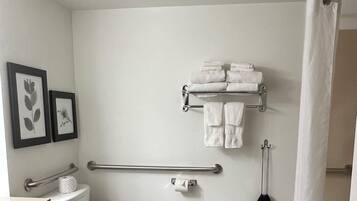 A bathroom with a toilet, a sink, a shower, a grab bar, and a small step stool.