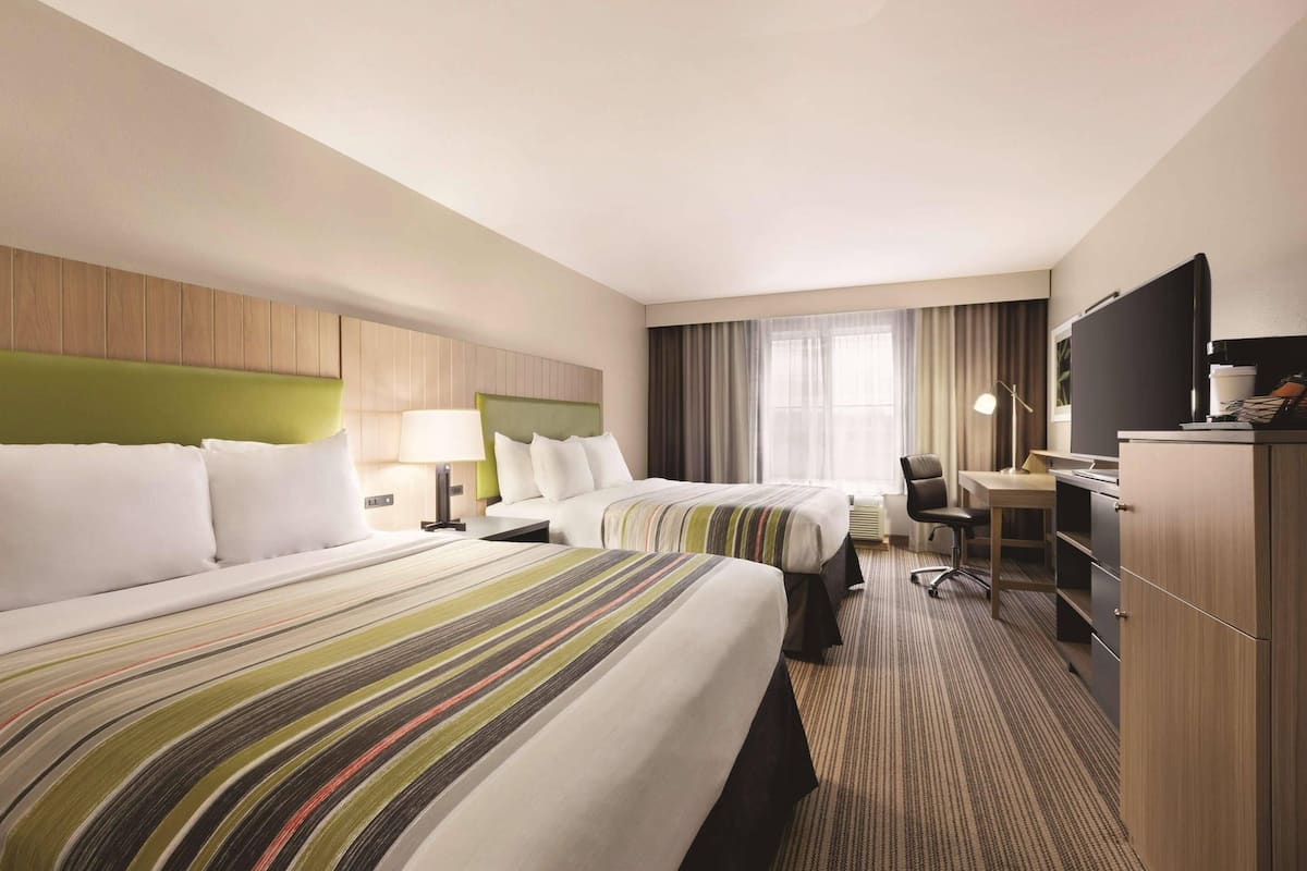 A hotel room with two beds, a desk, a chair, a television, and a wardrobe.