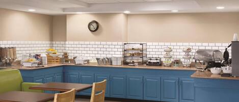 A kitchen with blue cabinets, a clock on the wall, and a breakfast bar with various food items.