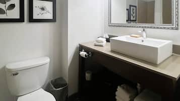 A bathroom with a toilet, sink, mirror, framed pictures, and a trash bin.