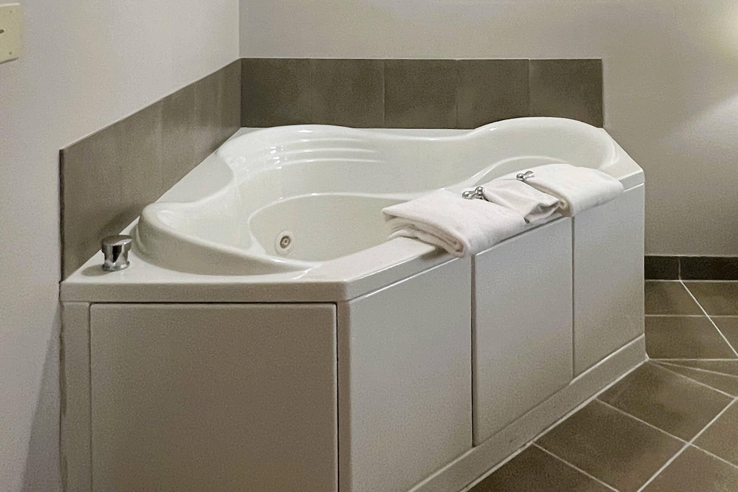 A corner bathtub with a towel on it, a faucet, and a control knob.