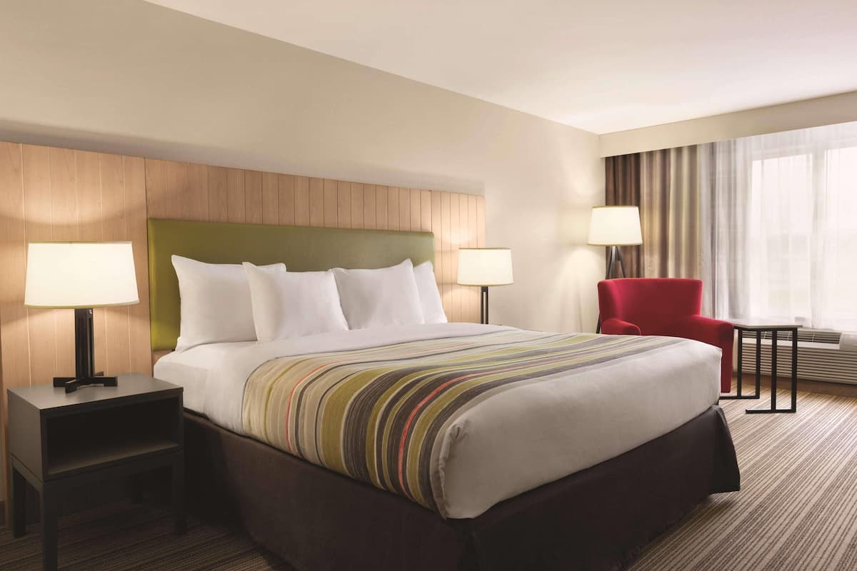 A hotel room with a bed, two bedside tables with lamps, a red chair, and a window with curtains.