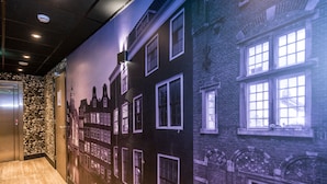 Un pasillo con un mural de una fachada de edificio, piso de madera y un ascensor.