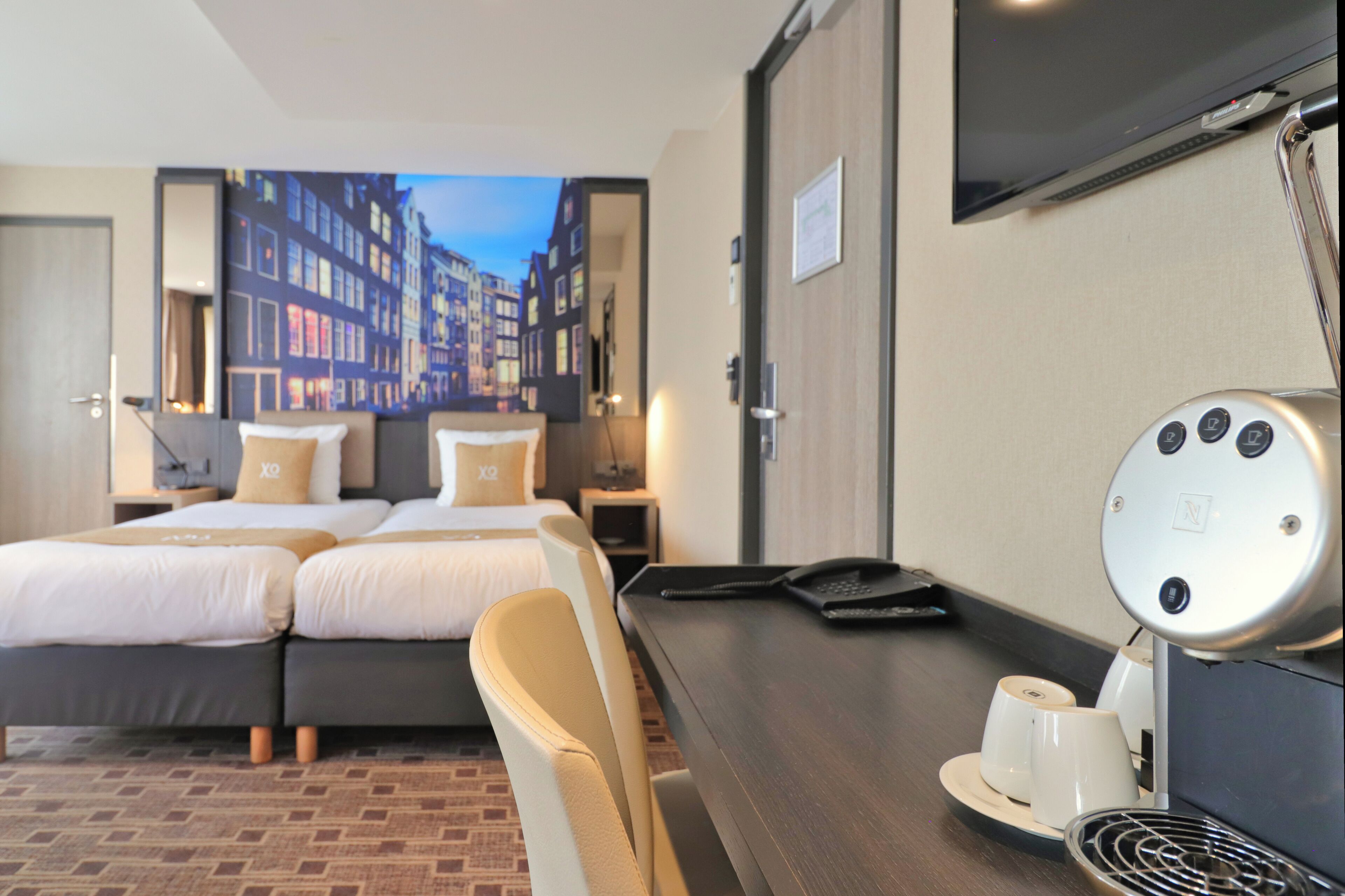 A hotel room with a bed, a desk, a chair, a coffee machine, and a television.