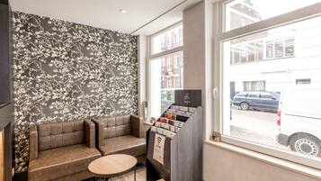 Eine moderne Lobby mit einer Couch, einem kleinen Tisch, einer digitalen Kiosk und Blick auf die Straße durch ein großes Fenster.