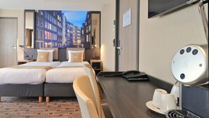 Habitación de hotel con cama, escritorio, silla, cafetera y televisión.