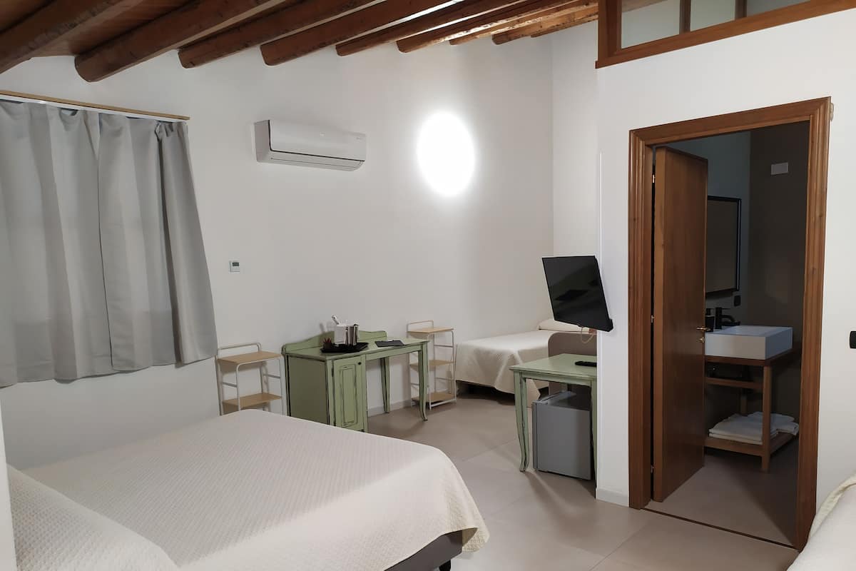 Un dormitorio con dos camas, un escritorio, un televisor y un baño que se ve a través de una puerta abierta.