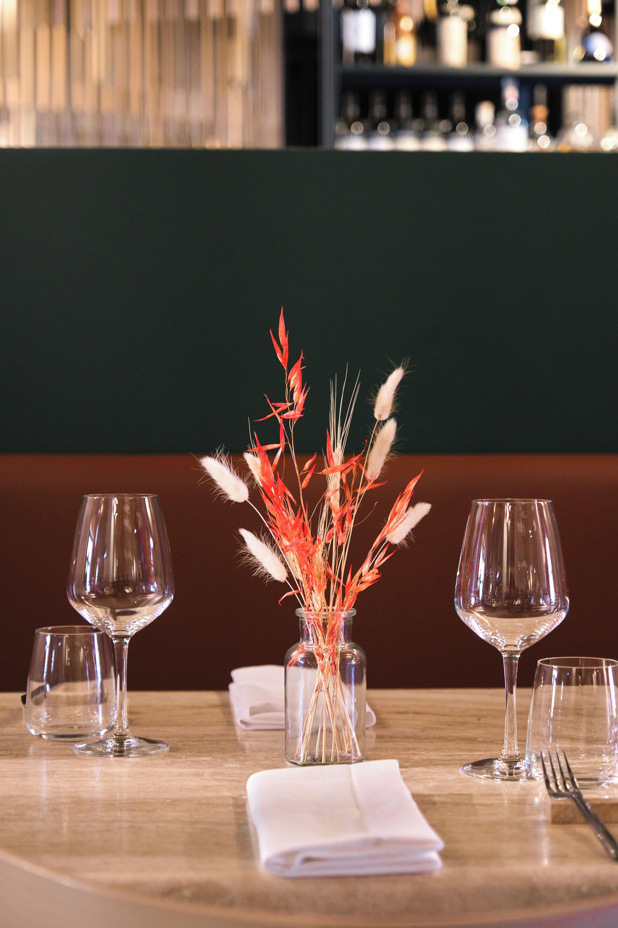 A dining table with a vase of decorative plants, two wine glasses, a folded napkin, and a fork.