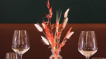 A dining table with a vase of decorative plants, two wine glasses, a folded napkin, and a fork.
