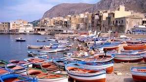 A harbor with numerous small boats docked along the shore, surrounded by buildings and a mountainous backdrop. - Villa Scaduto Residence (Bagheria)