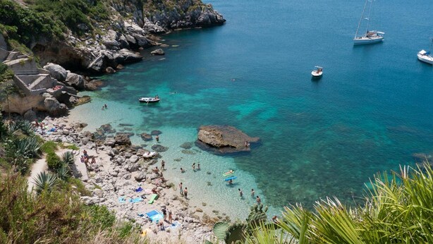 A coastal area with clear turquoise waters, rocky shore, and a few boats. - Villa Scaduto Residence (Bagheria)