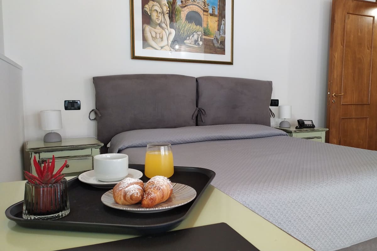 Una habitación de hotel con cama, una bandeja con croissants y jugo de naranja, un cuadro en la pared y una puerta de madera.